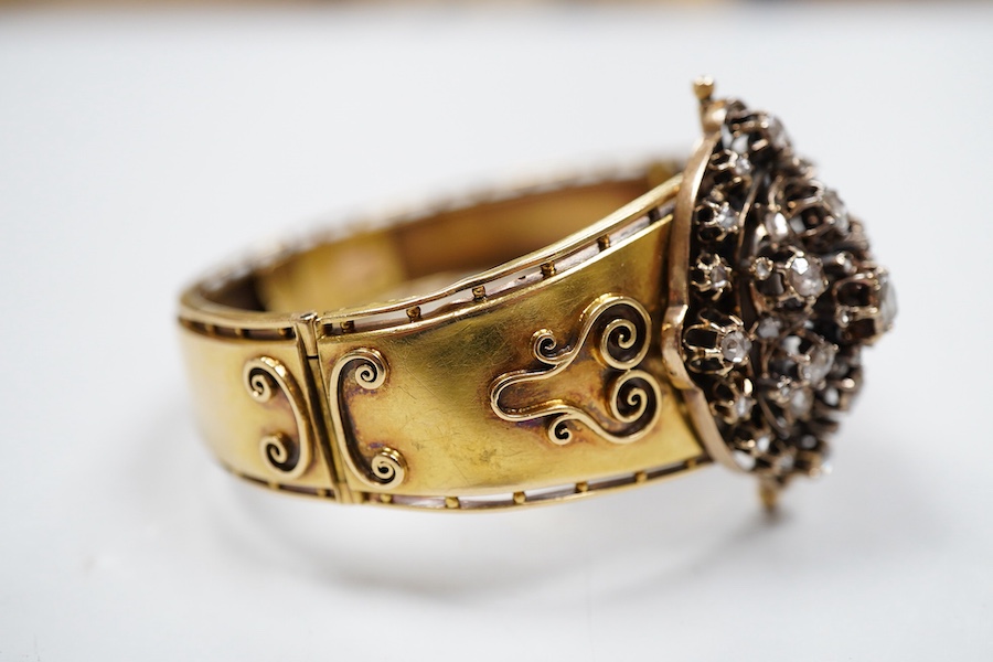 A Victorian gold and diamond bracelet, the hinged cuff decorated with wire scrollwork, centring on an oval motif set with rose-cut diamonds, inner circumference approximately 17cm, width at front 3.8cm, gross weight appr